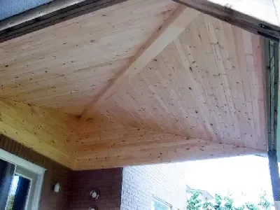 A view looking up at a newly installed light-colored wood plank ceiling on a home's outdoor porch.