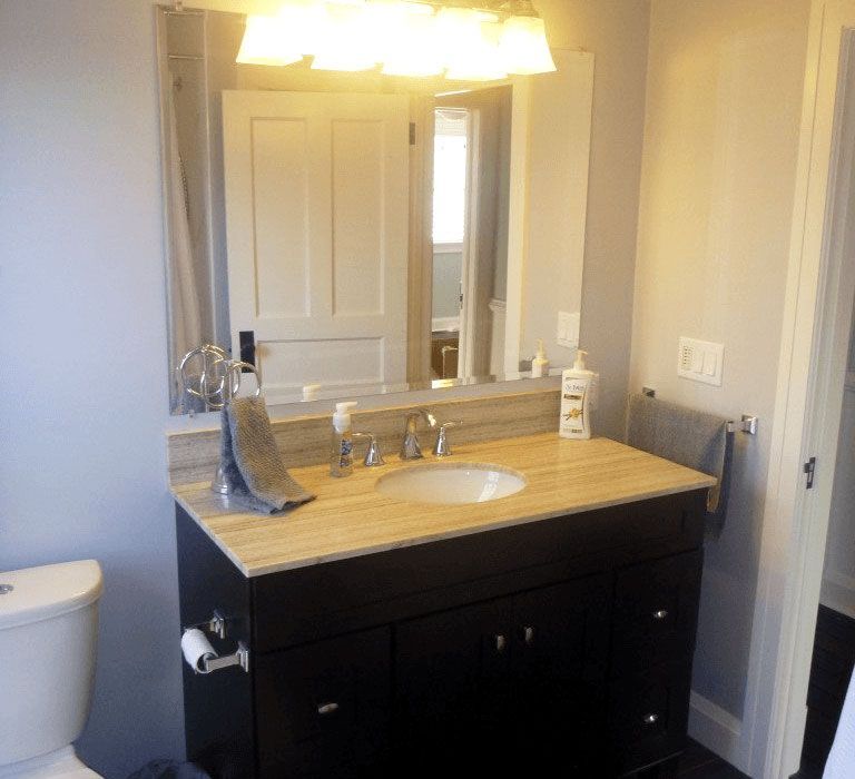 A bathroom vanity with a dark wood cabinet, beige stone countertop, white sink, mirror, and a light fixture overhead.
