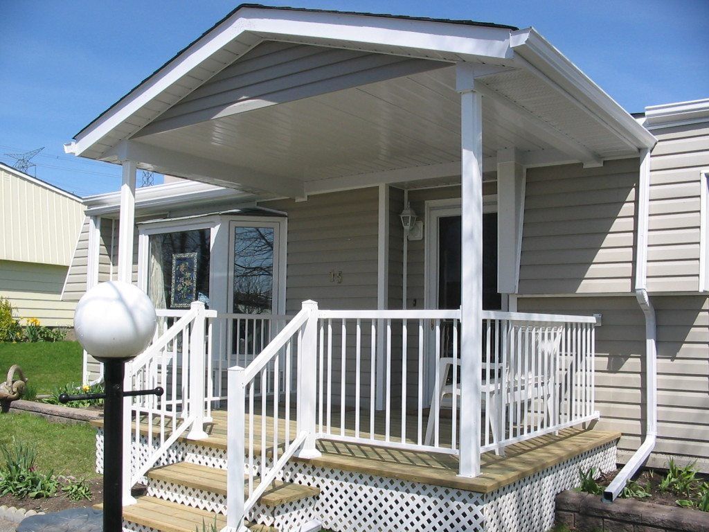 A tan mobile home with a white covered porch, a white railing, and wooden steps, next to a black lamp post.