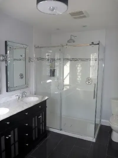 Modern bathroom with a black vanity, white marble countertop, and a glass-enclosed shower on a dark tiled floor.