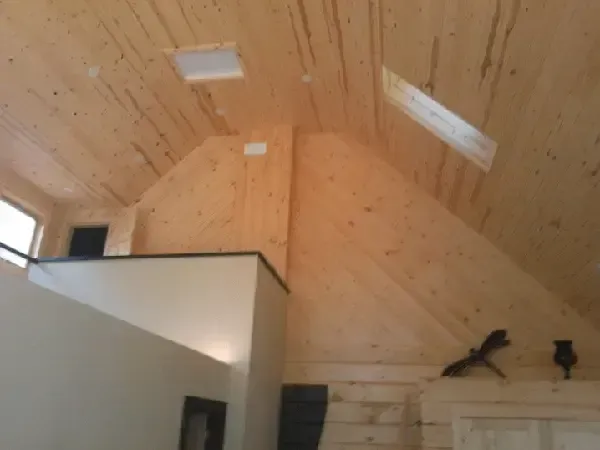 An interior view of a loft with a wooden vaulted ceiling, two skylights, and a white partition wall.