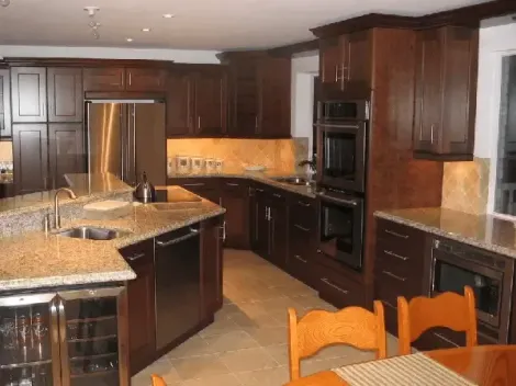 A kitchen with dark wood cabinets, stainless steel appliances, a granite-topped island, and a dining area.