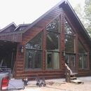 A dark wood-paneled cabin with large, tall triangular windows under construction, featuring a partially finished exterior.