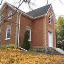 A two-story red brick building with white trim and a stone foundation, set among autumn leaves on a cloudy day.