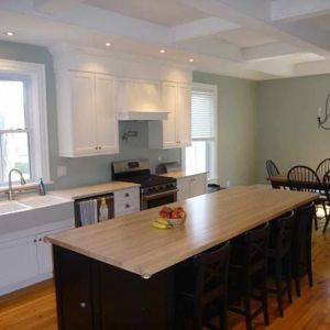 A spacious kitchen with white cabinets, a large island with a light wood countertop, and sage green walls.