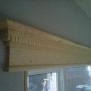 A decorative, light-colored wooden window valance with dentil molding mounted above a window.