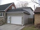 A two-story house addition featuring a stone-front garage, white door, and grey siding, attached to a brick home.