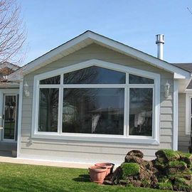 A light-colored house exterior with a large, multi-pane window and a pile of dirt and sod in the yard.