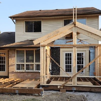 A house exterior showing a wooden frame addition under construction attached to the back of the building.