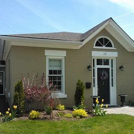A taupe, single-story house with a black front door, arched transom window, and a landscaped front yard with yellow tulips.