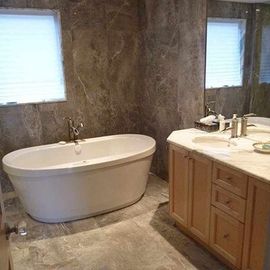 Modern bathroom with a white freestanding oval bathtub, wood vanity, and brown marble walls and flooring.