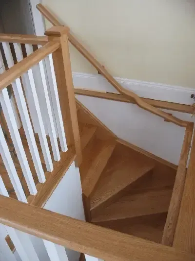 A wooden staircase featuring a winder section and a handrail attached to a light-colored wall.