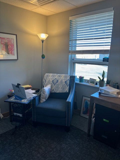 A room with a chair , desk , lamp and window.