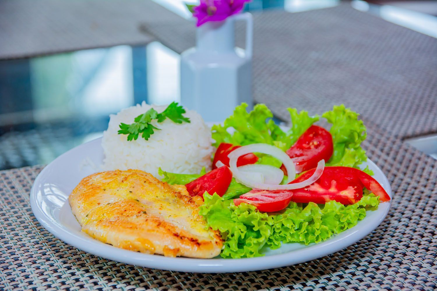 Um prato de comida com arroz, tomate, alface e cebola sobre uma mesa.