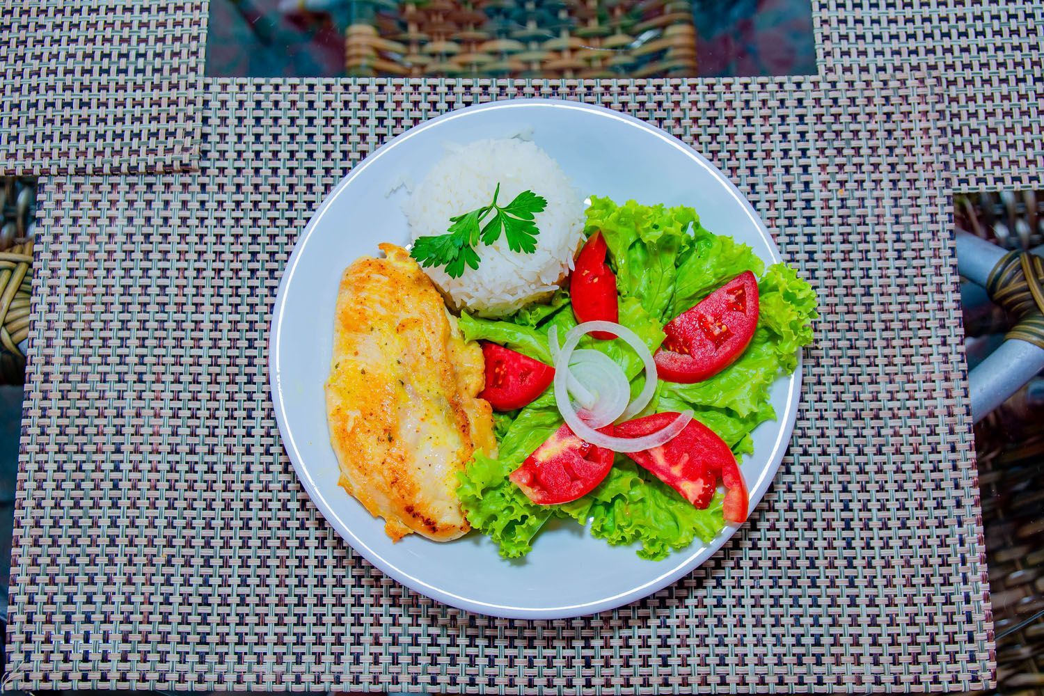 Um prato de comida com arroz, tomate, alface e cebola sobre uma mesa.