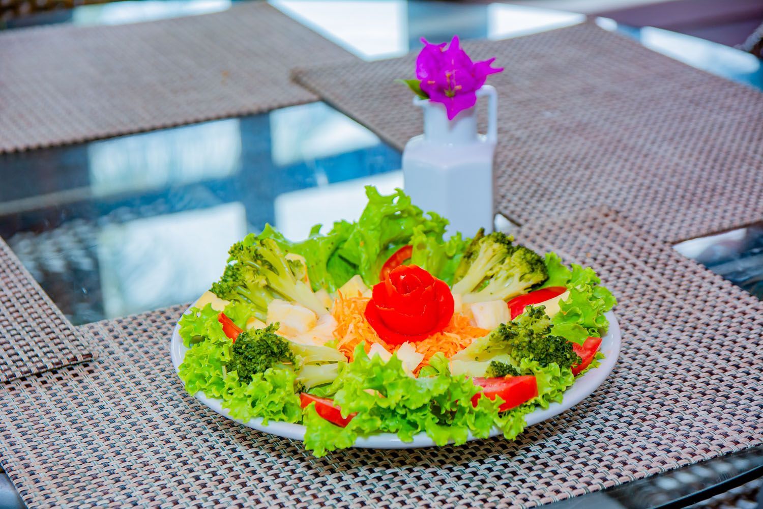 Um prato de salada com brócolis, alface, cenoura e tomate em uma mesa.