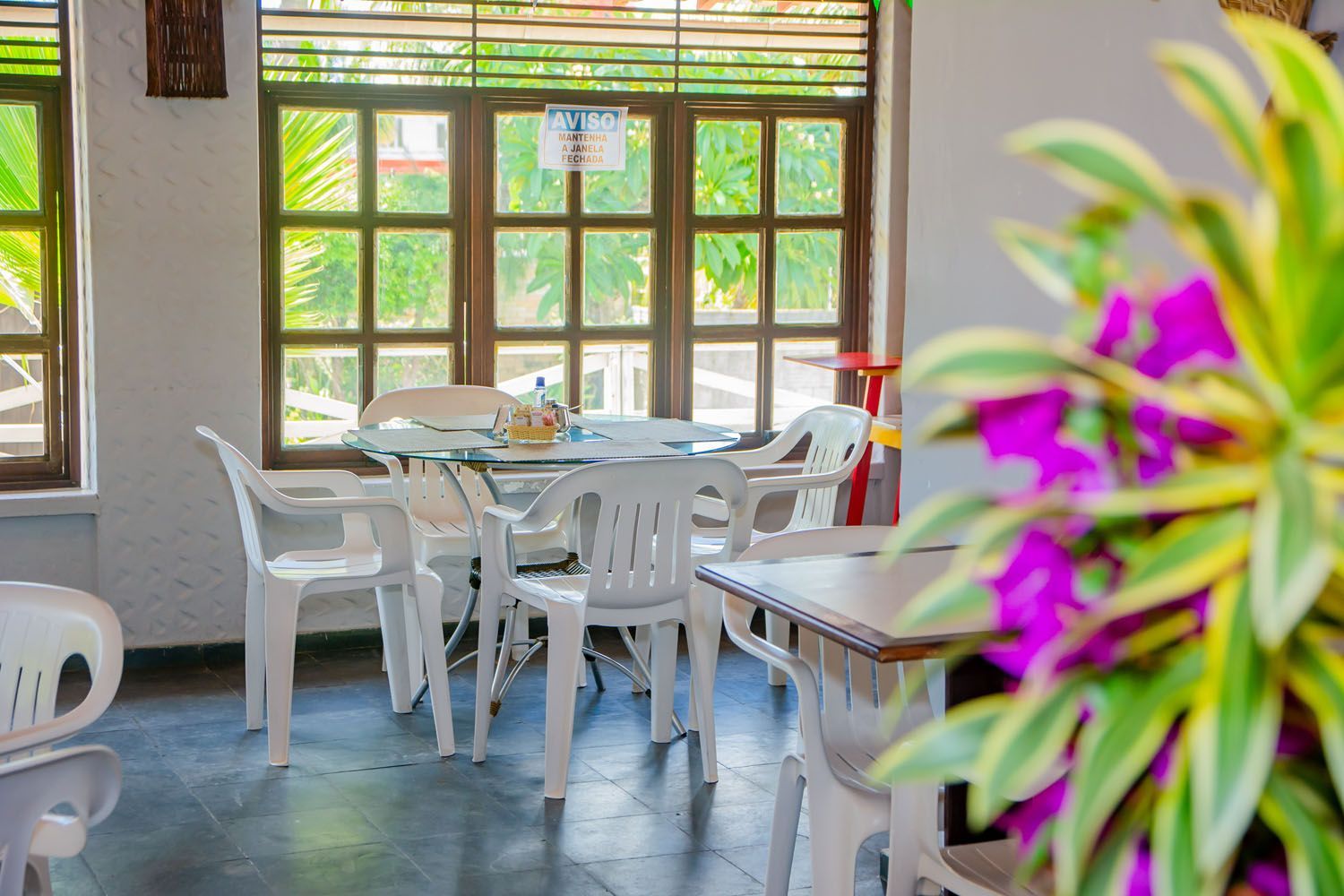 Uma sala com mesas e cadeiras e uma flor roxa em primeiro plano.