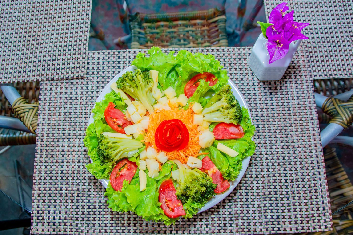 Um prato de salada com alface, brócolis, tomate e queijo sobre uma mesa.