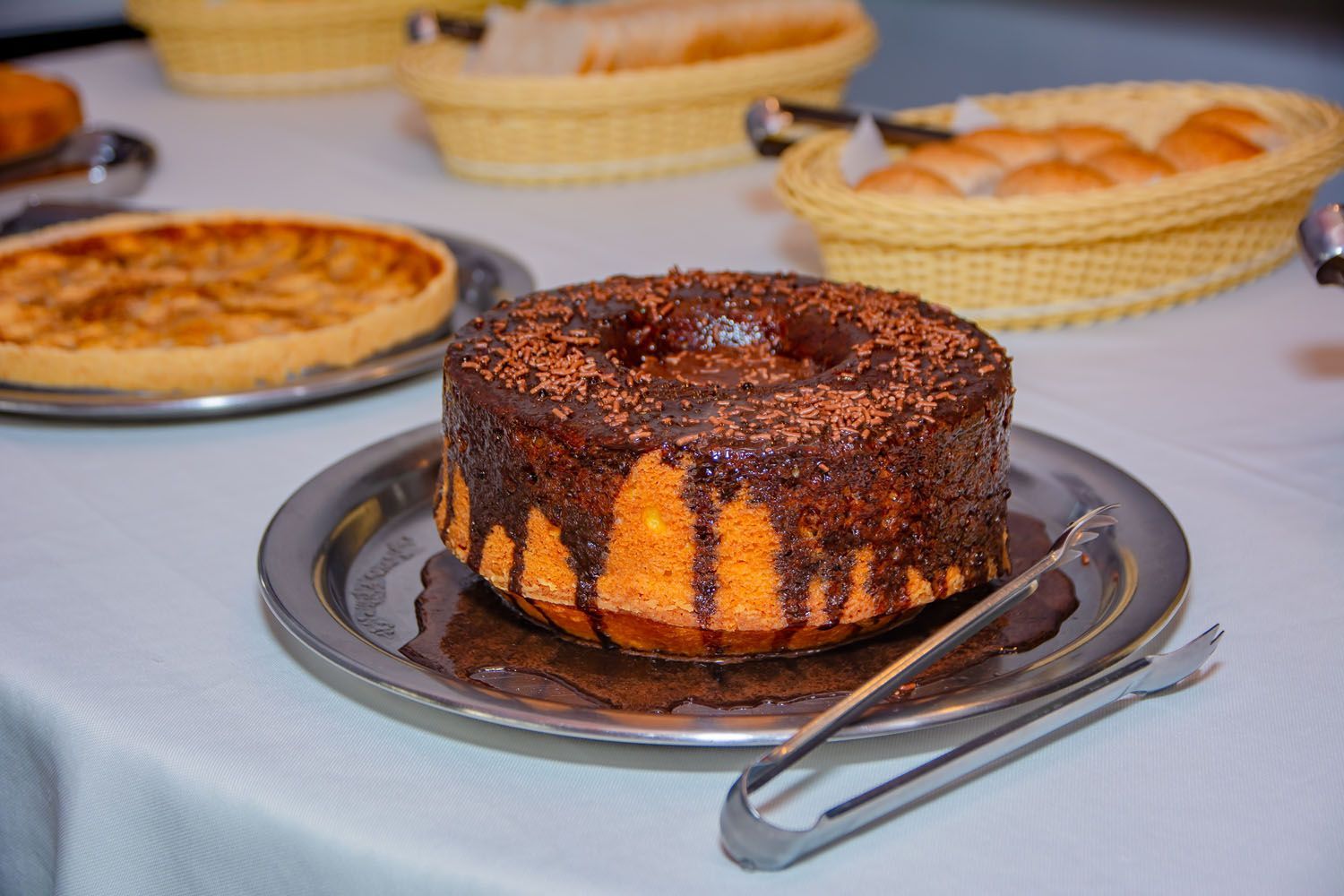 Um bolo de chocolate em um prato com pinças sobre uma mesa.