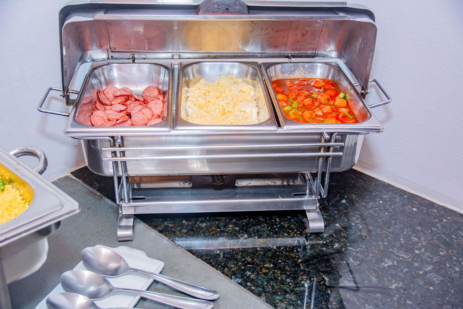 Um buffet repleto de comida e utensílios em um balcão.