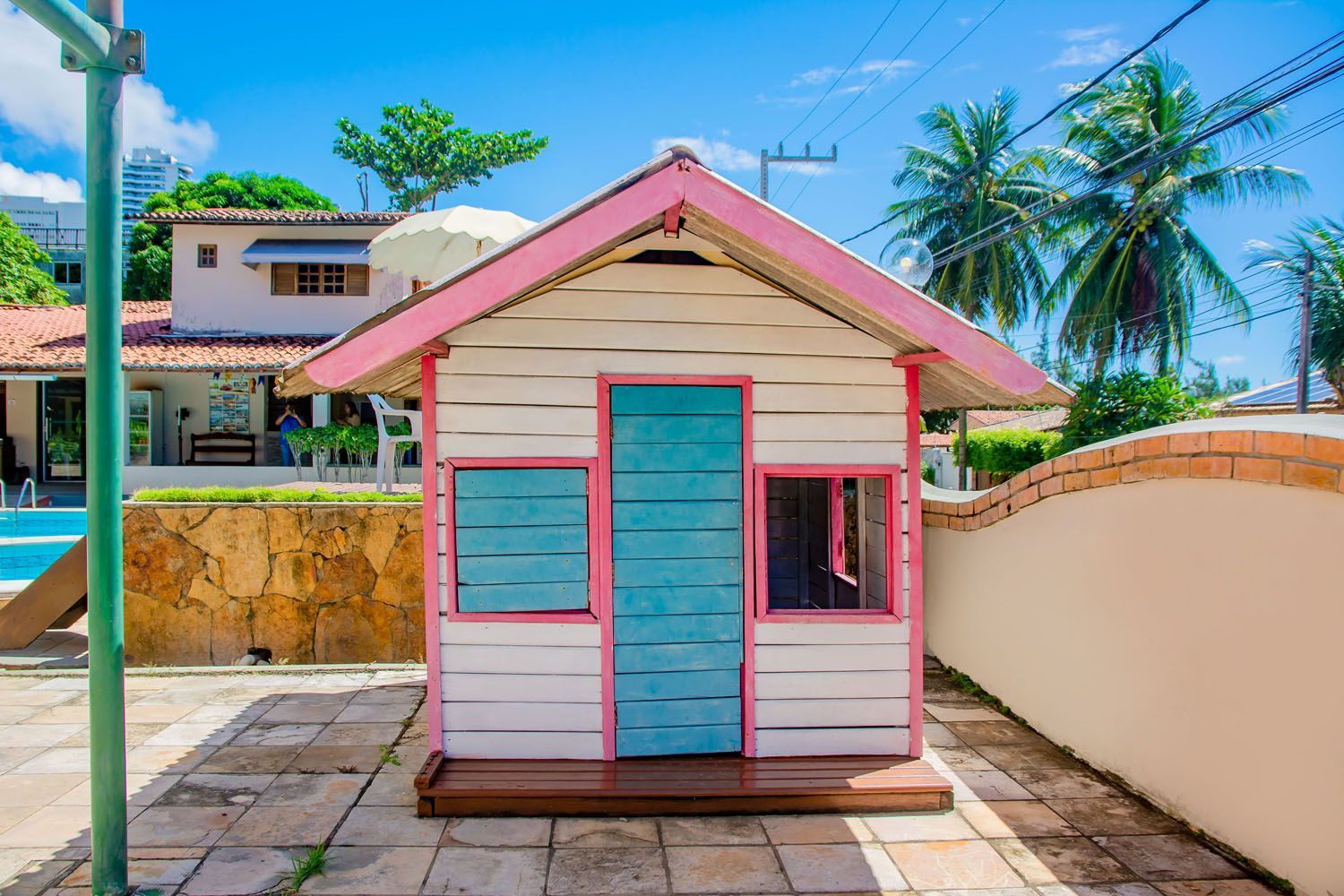 Um teatro rosa e branco com uma porta azul está na frente de uma casa.