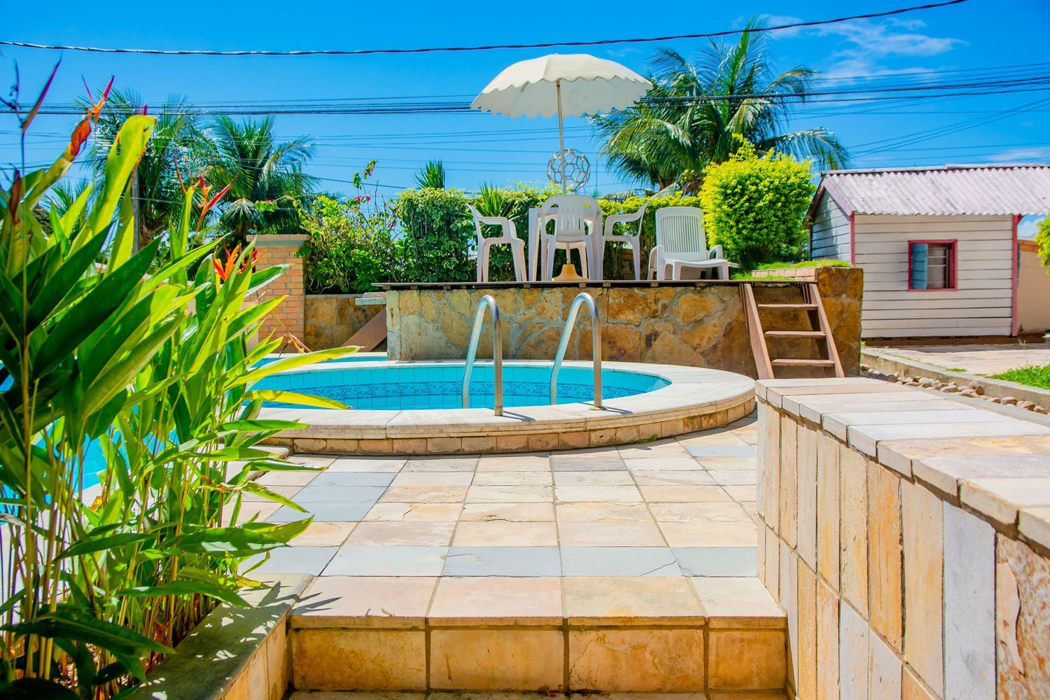 Uma piscina com um guarda-sol branco e cadeiras ao redor.