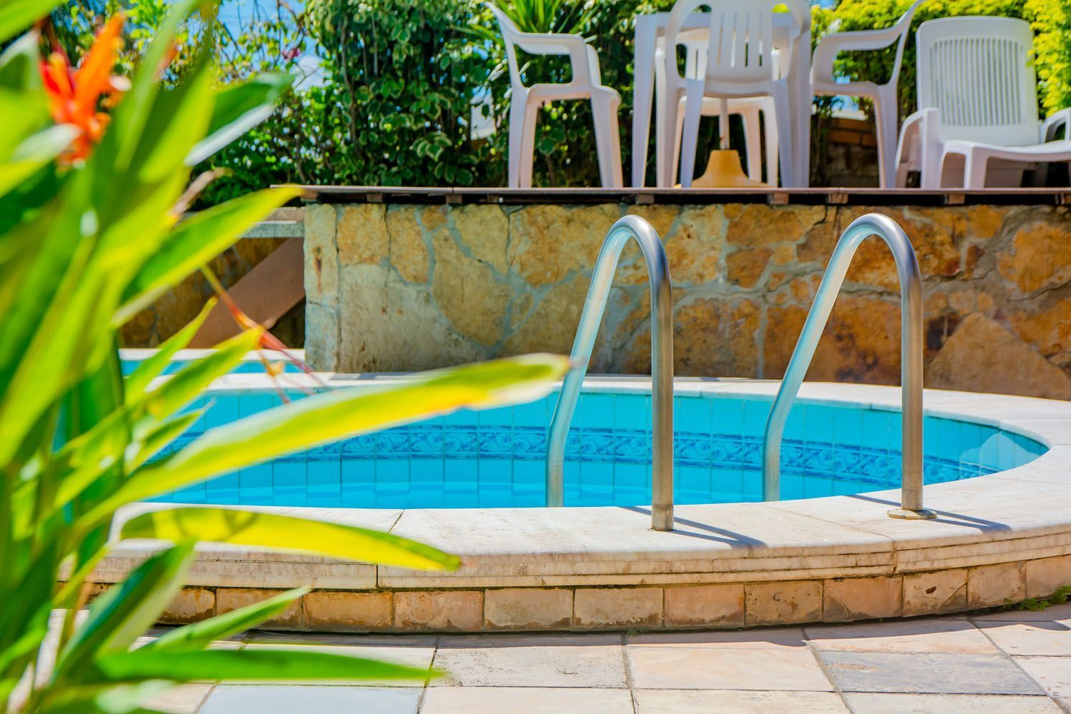 Uma piscina com escadas que levam até ela e cadeiras ao fundo.