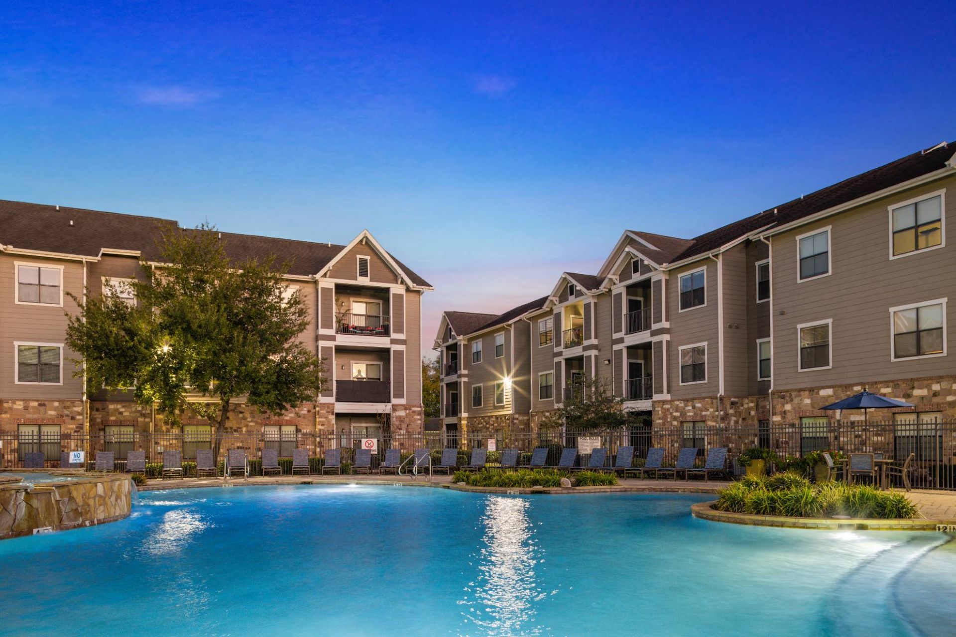 Outdoor apartment pool with lounge chairs and surrounding multi-story buildings.