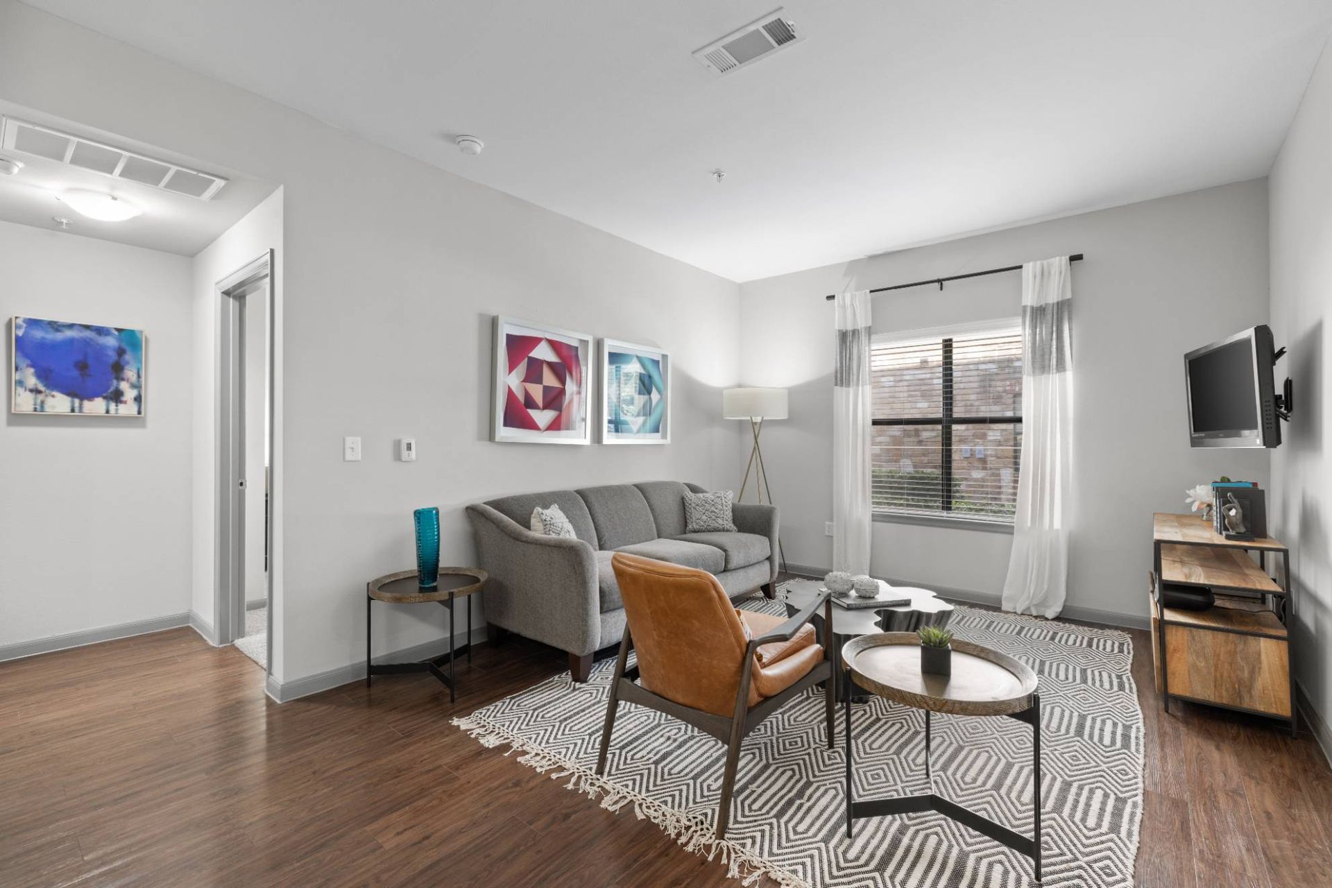 Living room in a modern apartment with sofa, chair, rug, and wall-mounted TV.