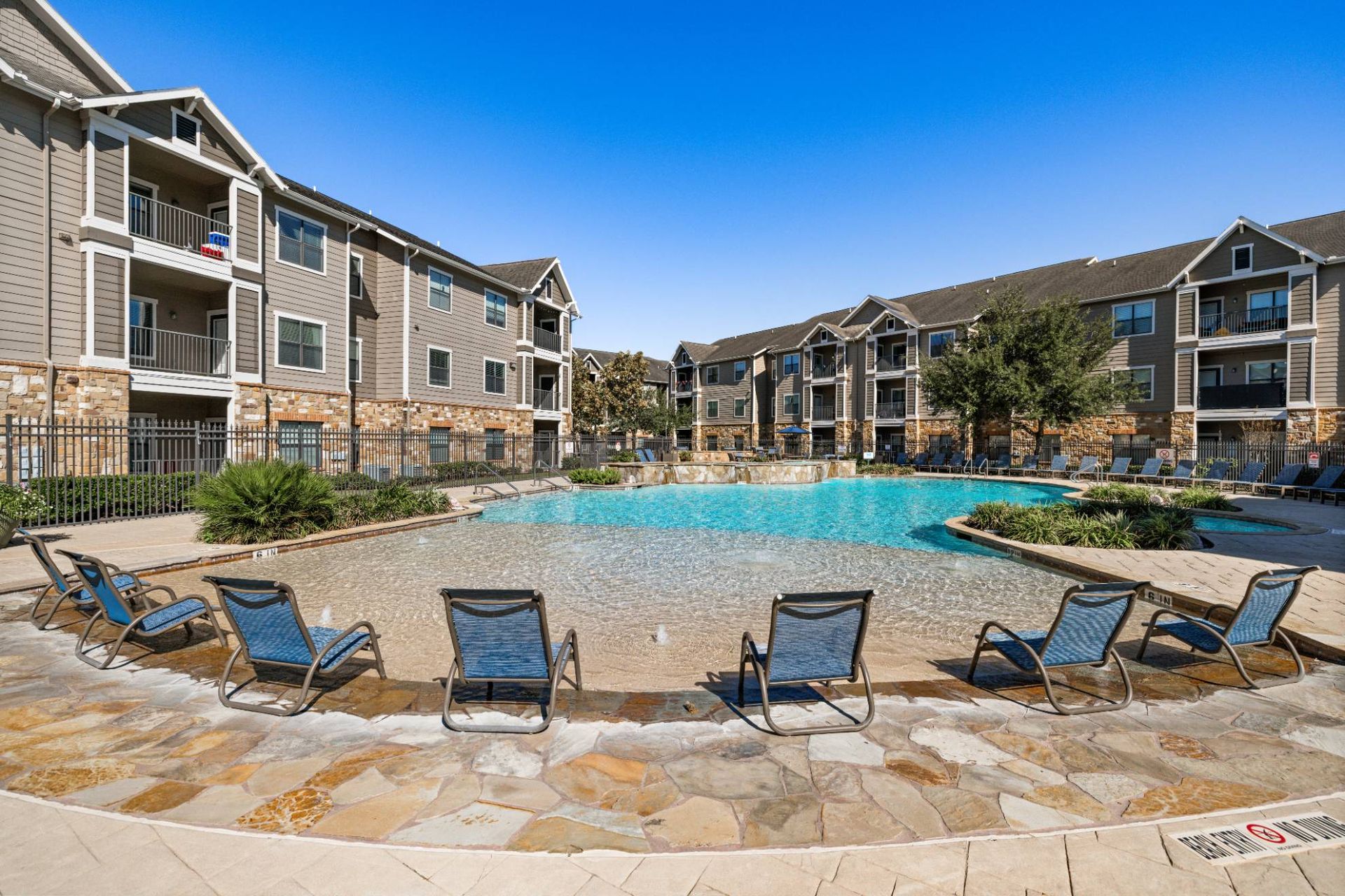Outdoor community pool with lounge chairs and surrounding apartment buildings.