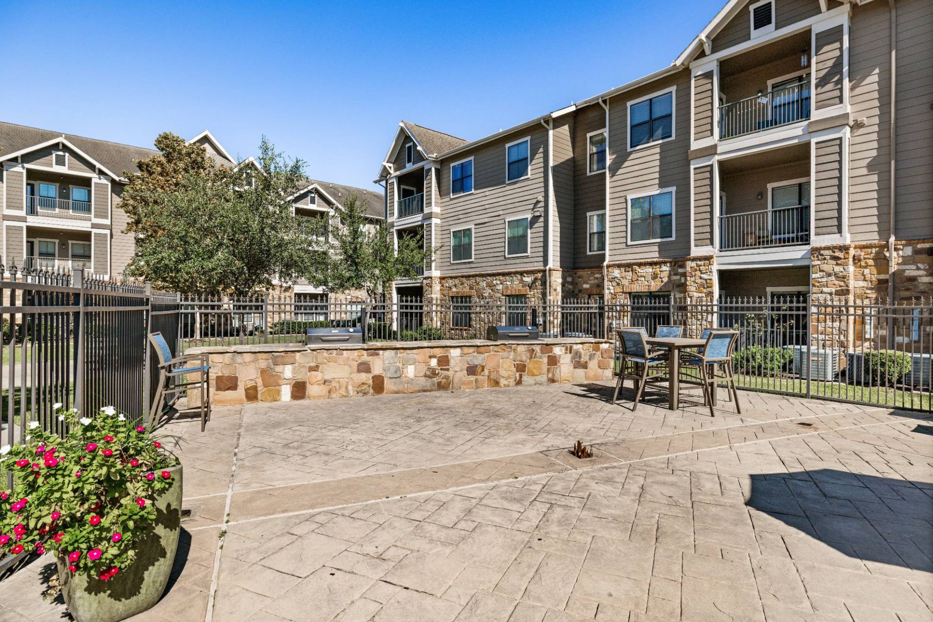 Community courtyard with stone seating wall, outdoor table and chairs, and apartment buildings in the background.