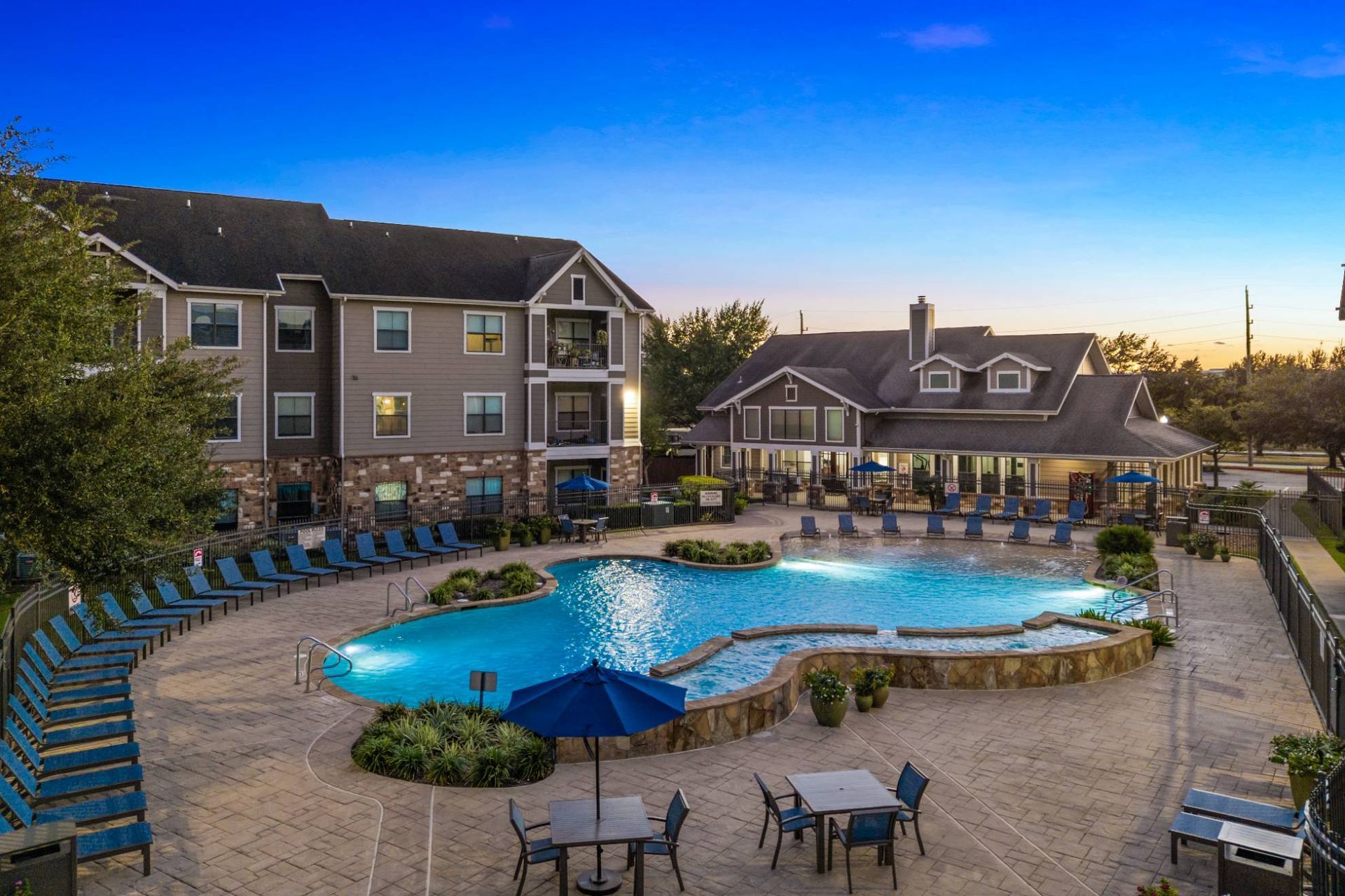Outdoor pool area at a multifamily community with lounge chairs and a clubhouse.