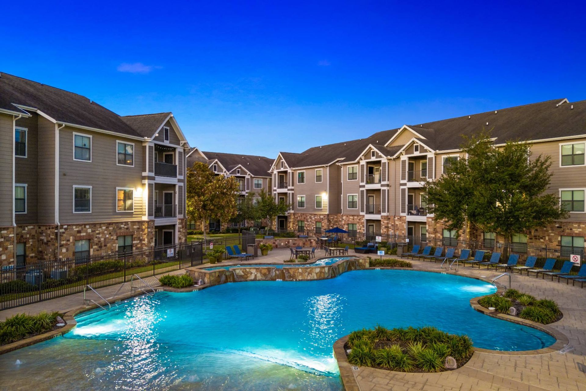 Outdoor pool area surrounded by apartment buildings and lounge chairs.