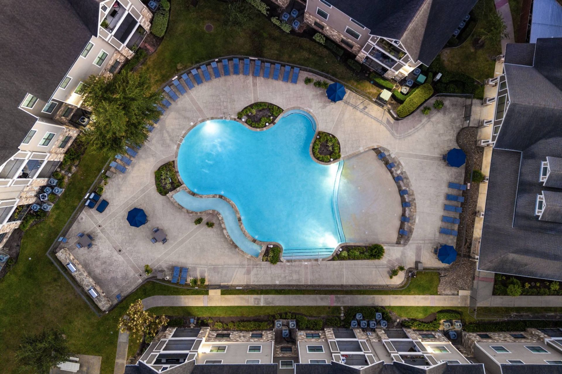 Aerial view of a curved blue pool surrounded by lounge chairs and apartment buildings.