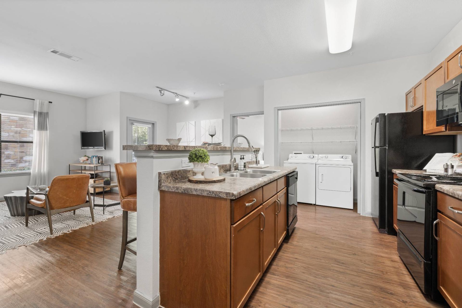 Open-concept kitchen with an island, wood cabinets, granite counters, and a nearby laundry area.