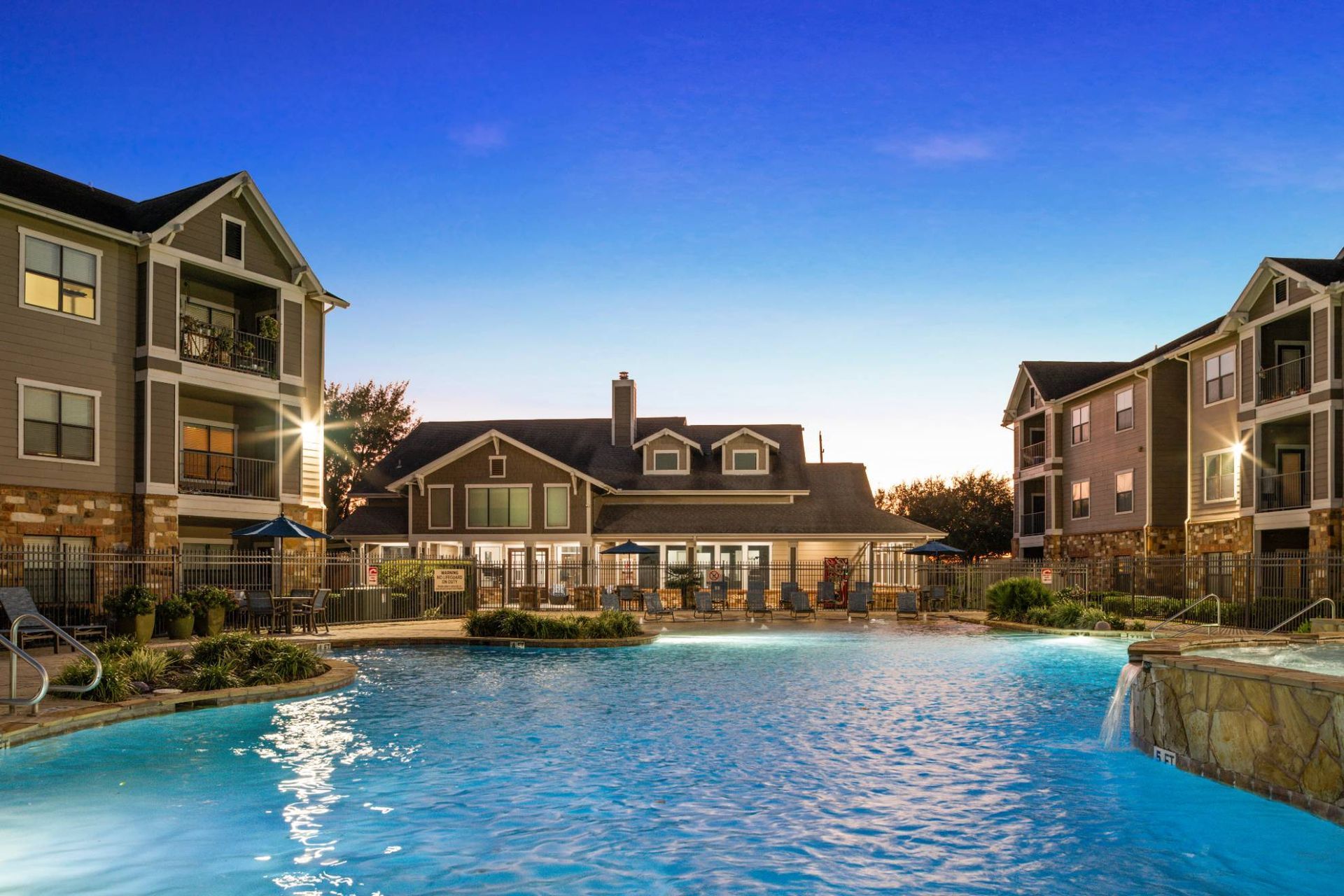 Outdoor apartment community pool with lounge chairs and surrounding buildings at dusk.
