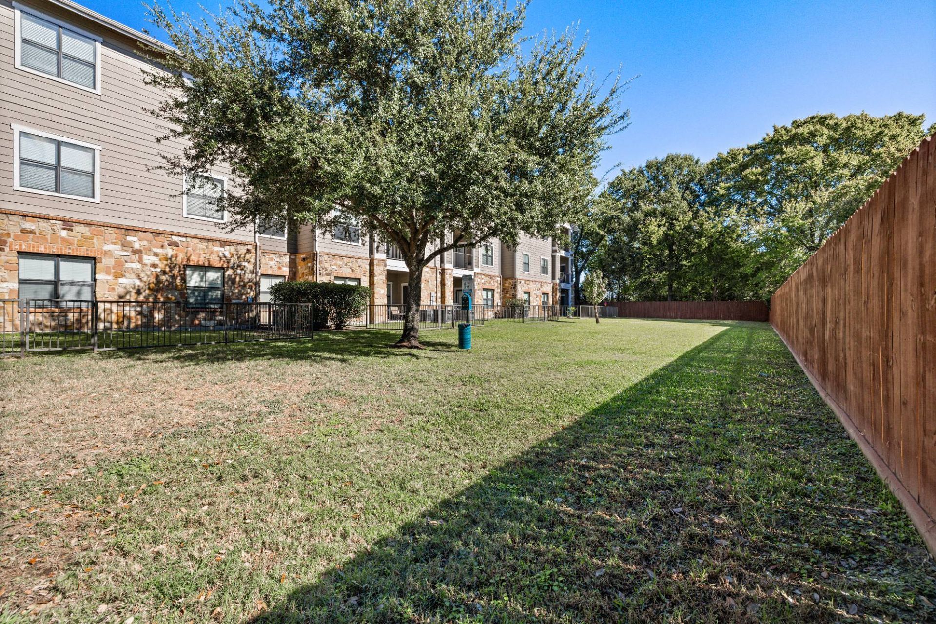 Exterior view of the apartment complex showing a grassy courtyard, trees, and a wooden fence.