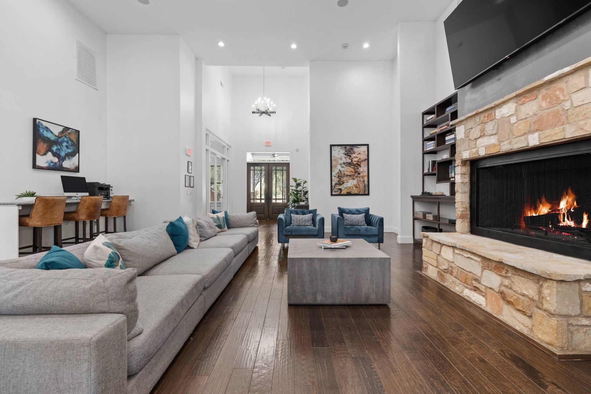 Spacious clubhouse living room with a sofa, blue chairs, a stone fireplace, and a mounted TV.