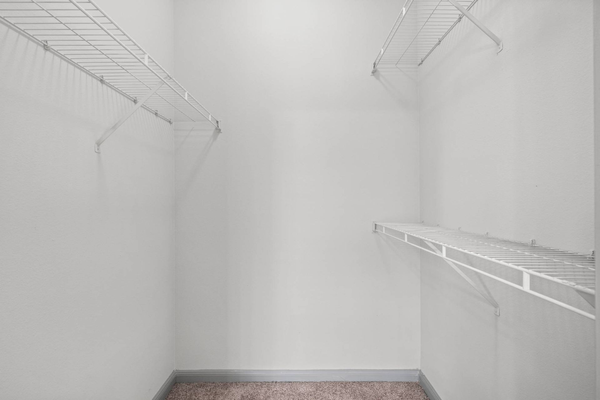 Walk-in closet with white wire shelving along two walls and a carpeted floor.