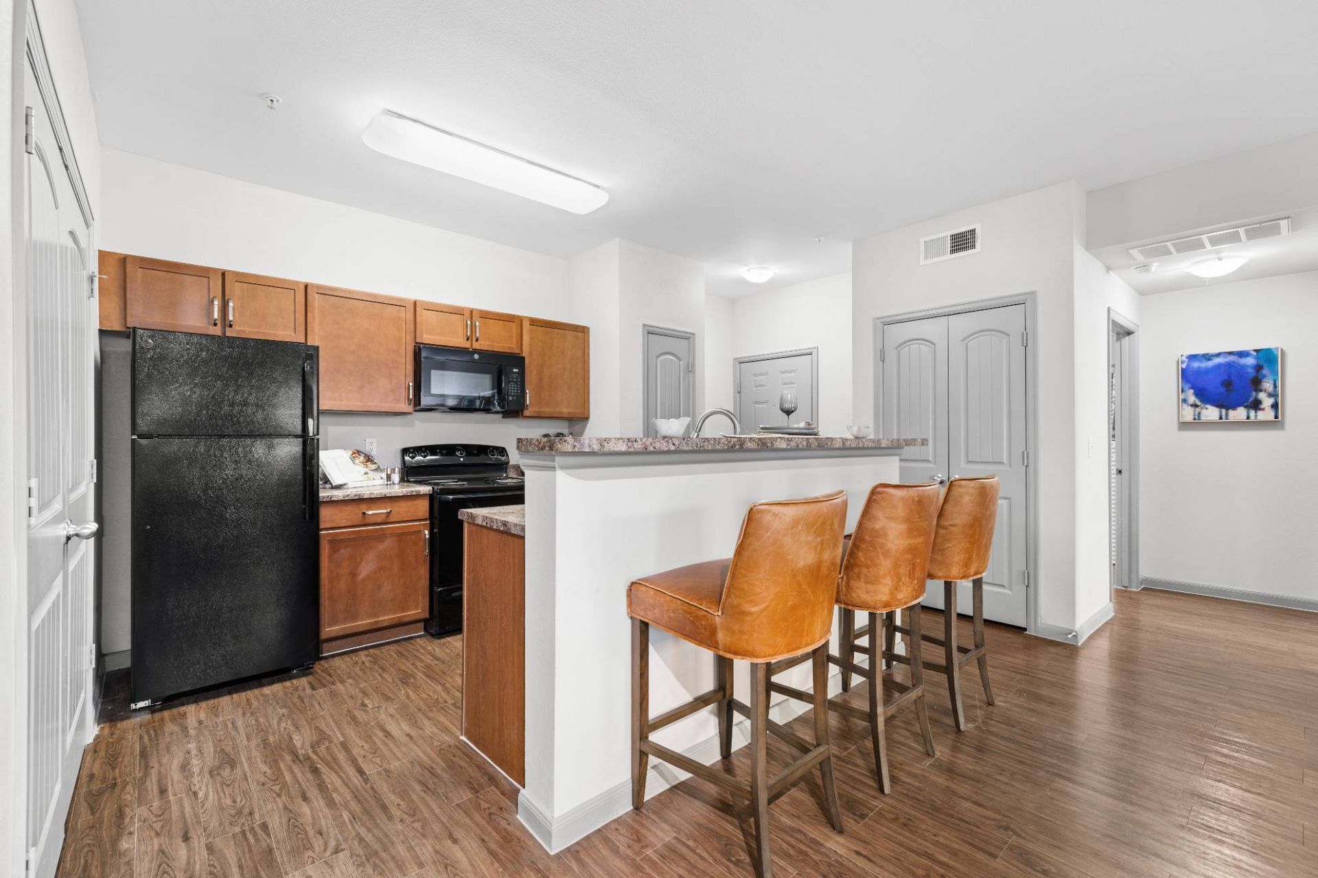 Kitchen in a modern apartment with wooden cabinets, black appliances, and a breakfast bar.
