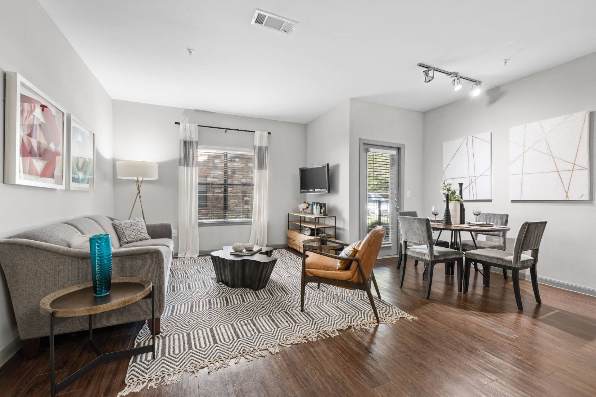 Open-concept apartment living room with gray sofa, armchair, coffee table, rug, TV, and dining area.