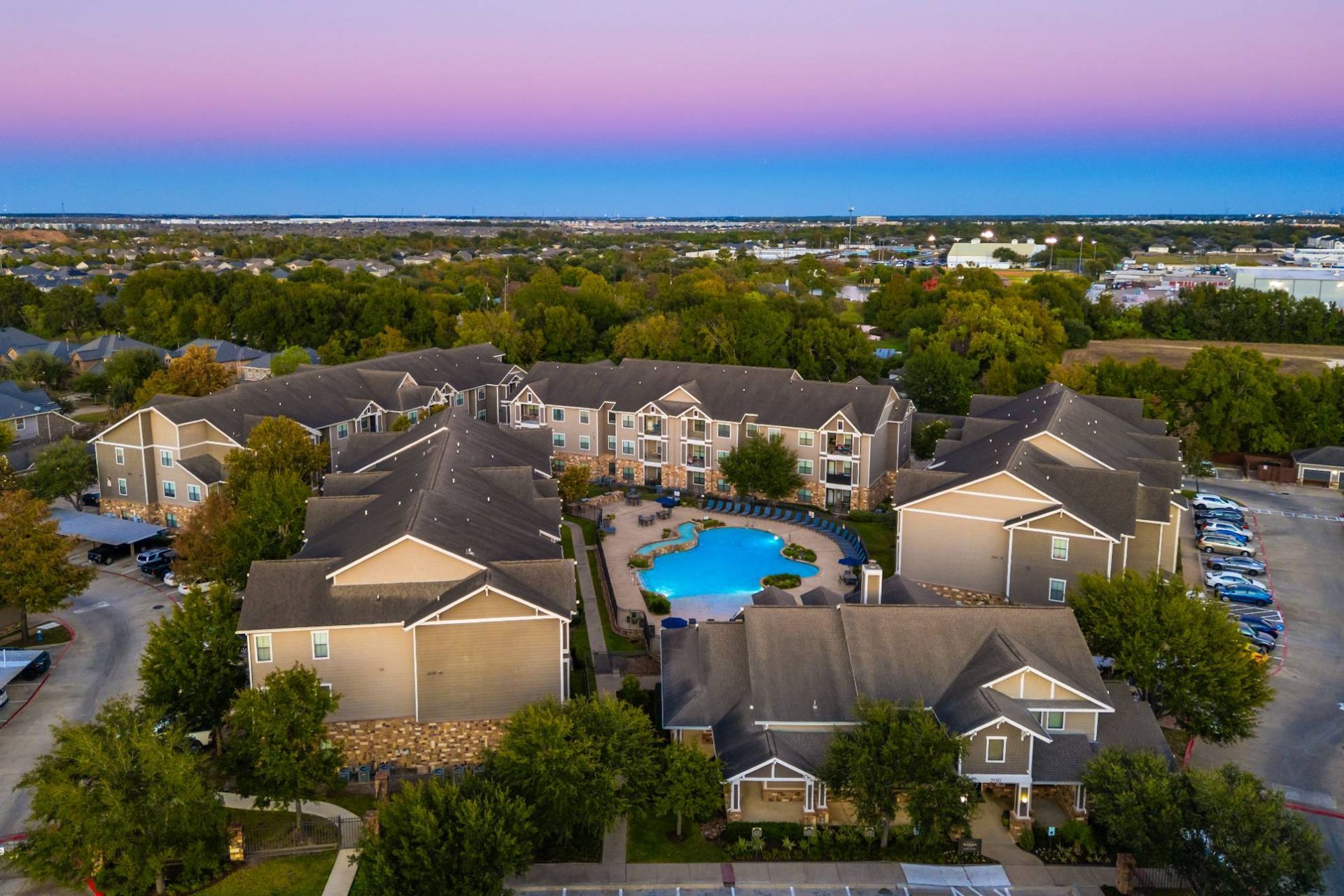 Aerial view of a multi-building apartment complex with a central pool and surrounding greenery.