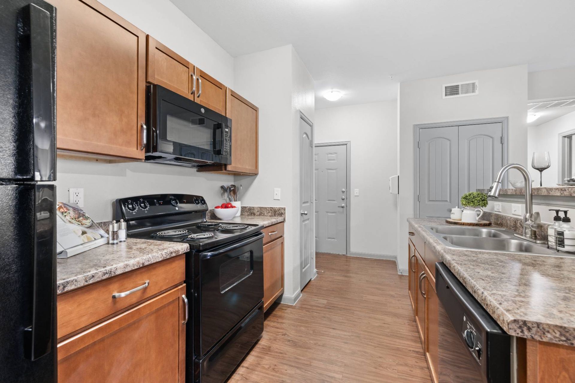 Kitchen with wood cabinets, black appliances, and a double sink at an island.