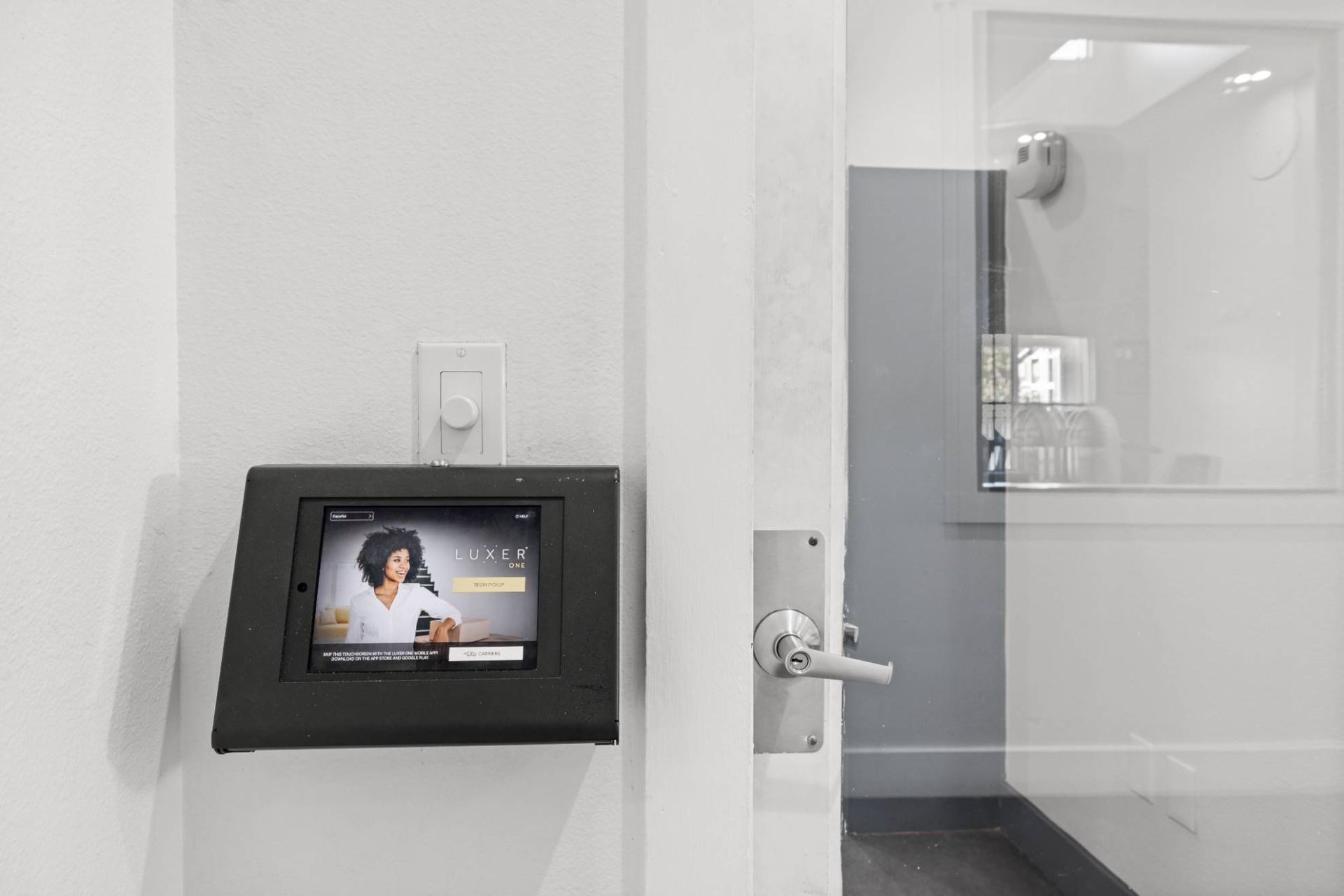 Wall-mounted touchscreen intercom panel at building entry beside a door.
