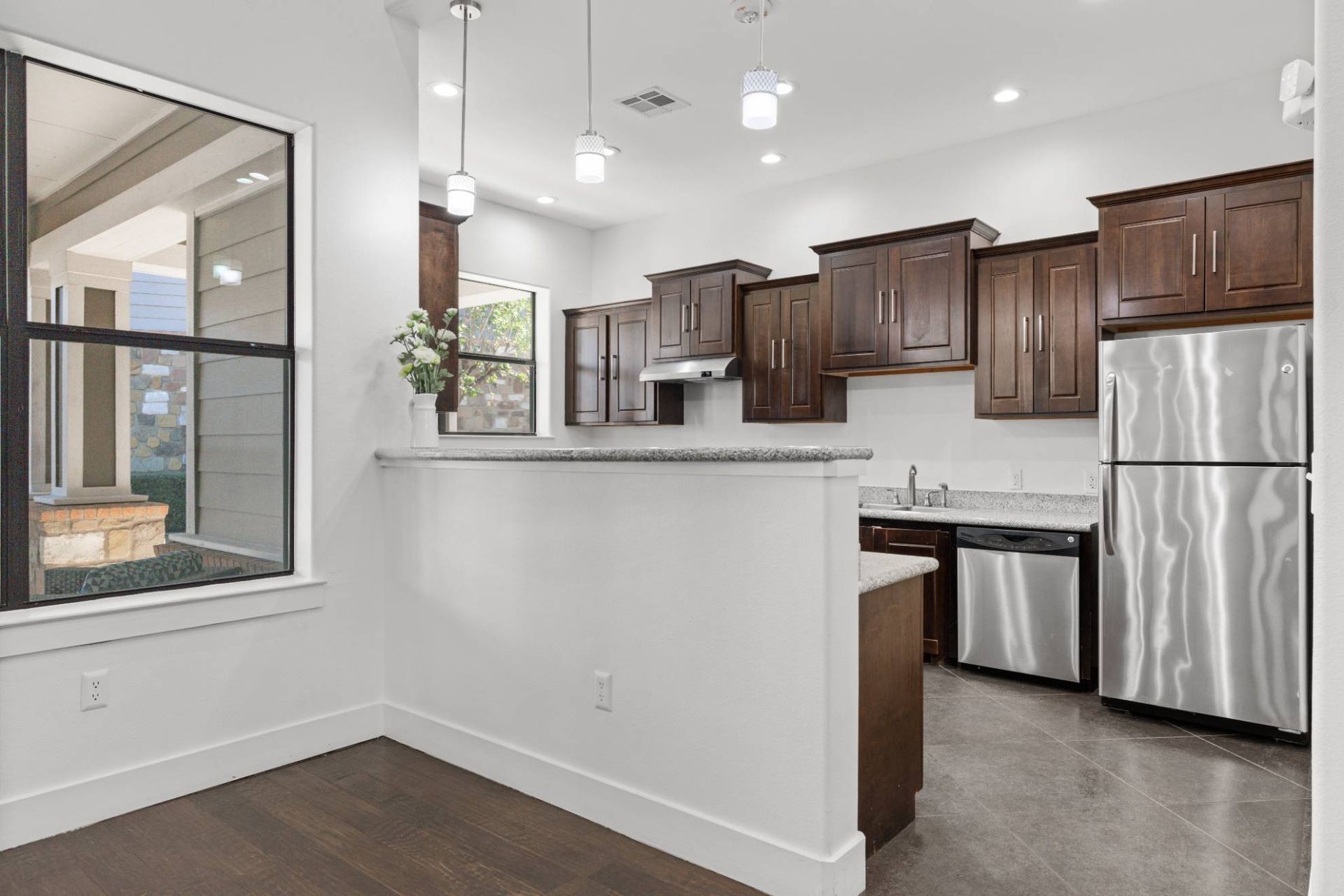 Modern apartment kitchen with dark wood cabinets, granite counters, and stainless steel appliances.