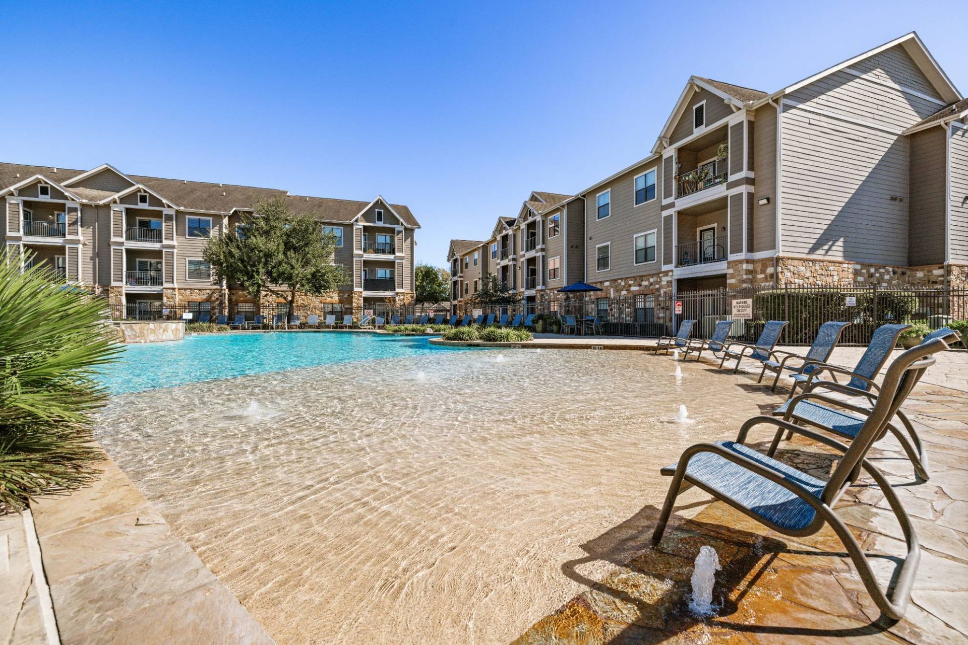 Outdoor community pool at apartment complex with lounge chairs and surrounding buildings.