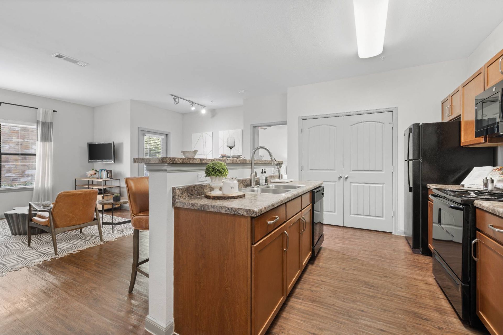 Open-concept apartment kitchen and living area with island, wood cabinets, and stainless appliances.