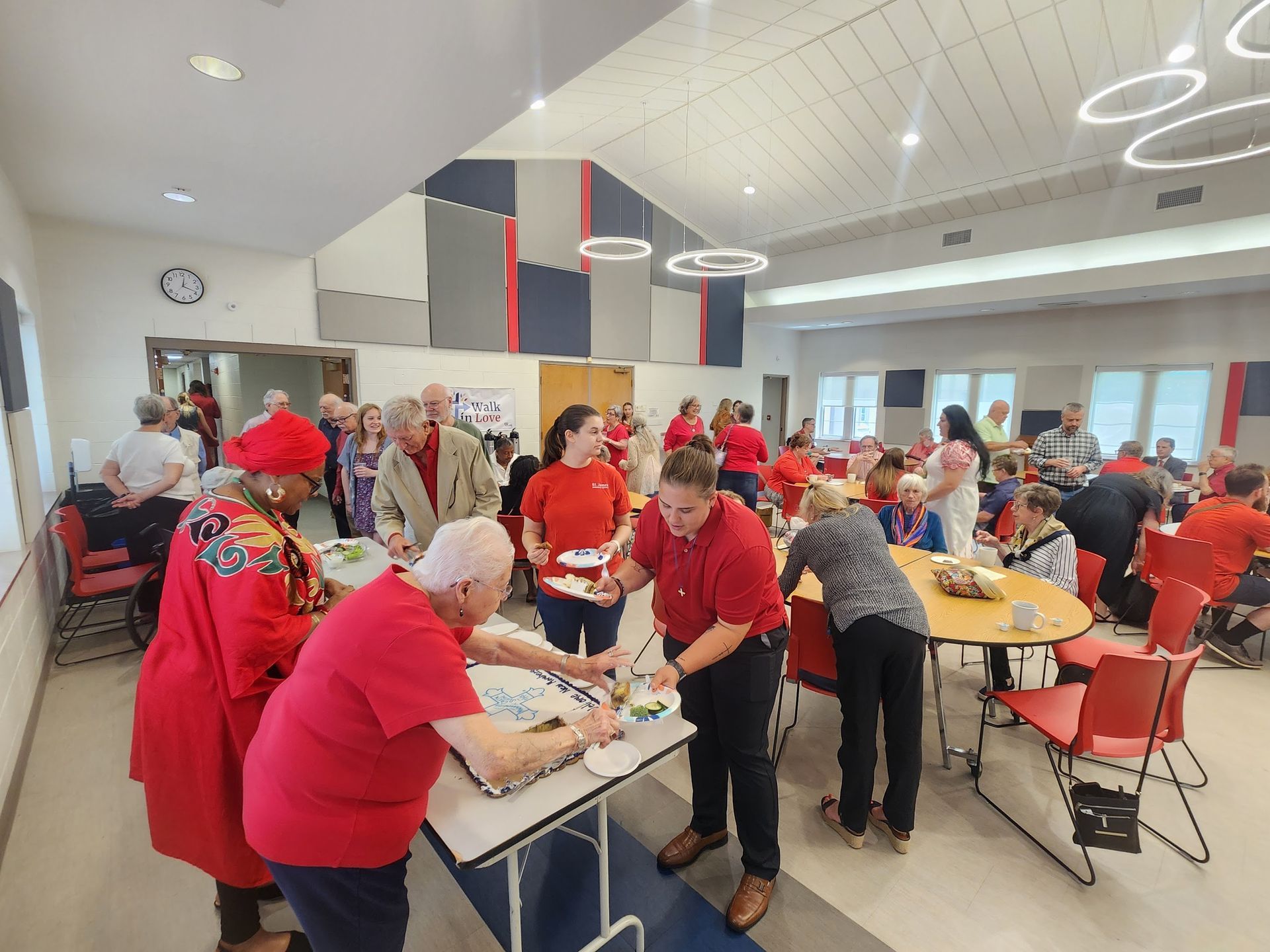 People in red shirts at an event in a large room with tables, food, and decorations.