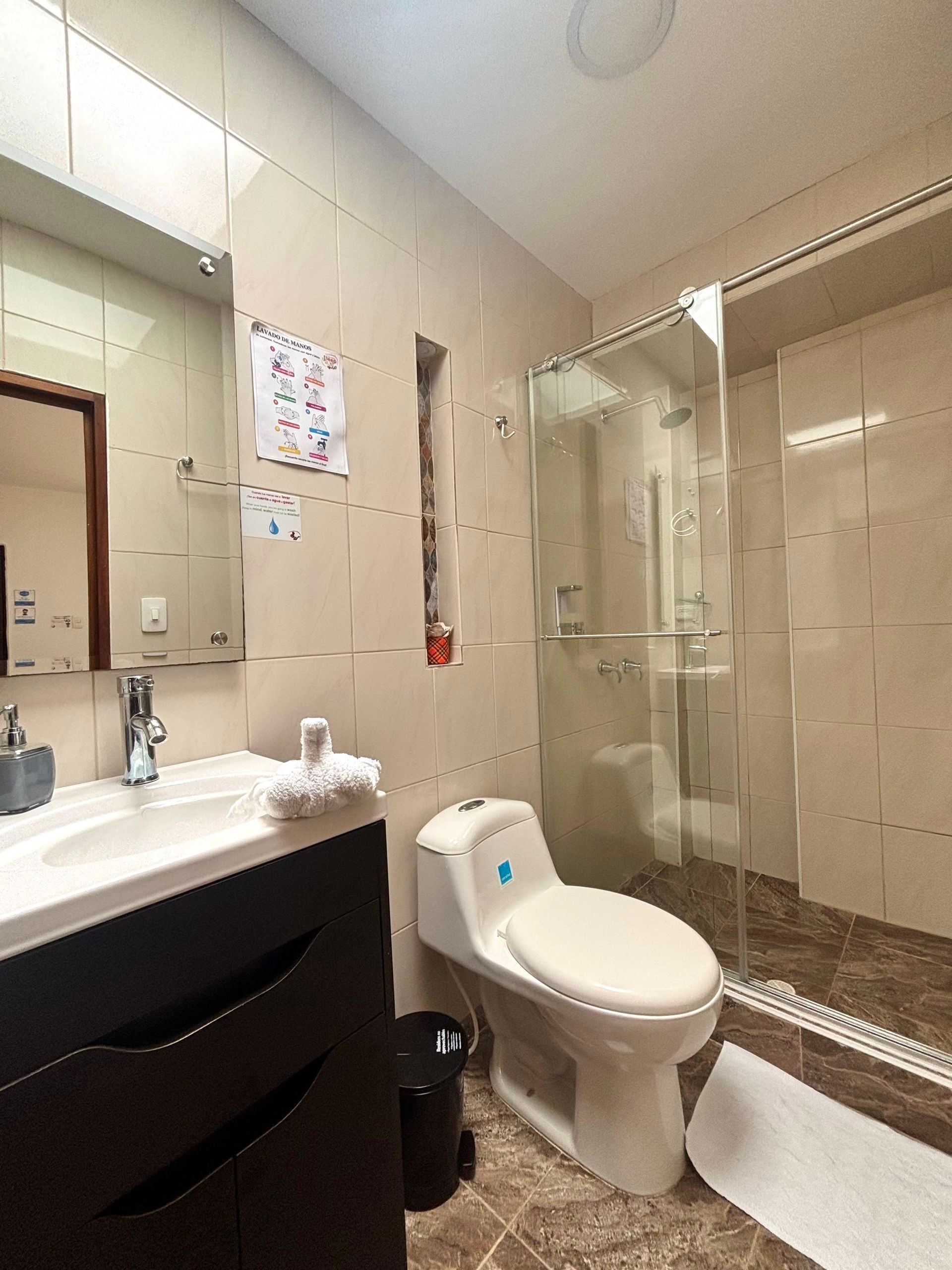 Baño pequeño con lavabo, inodoro y cabina de ducha de cristal a la derecha.
