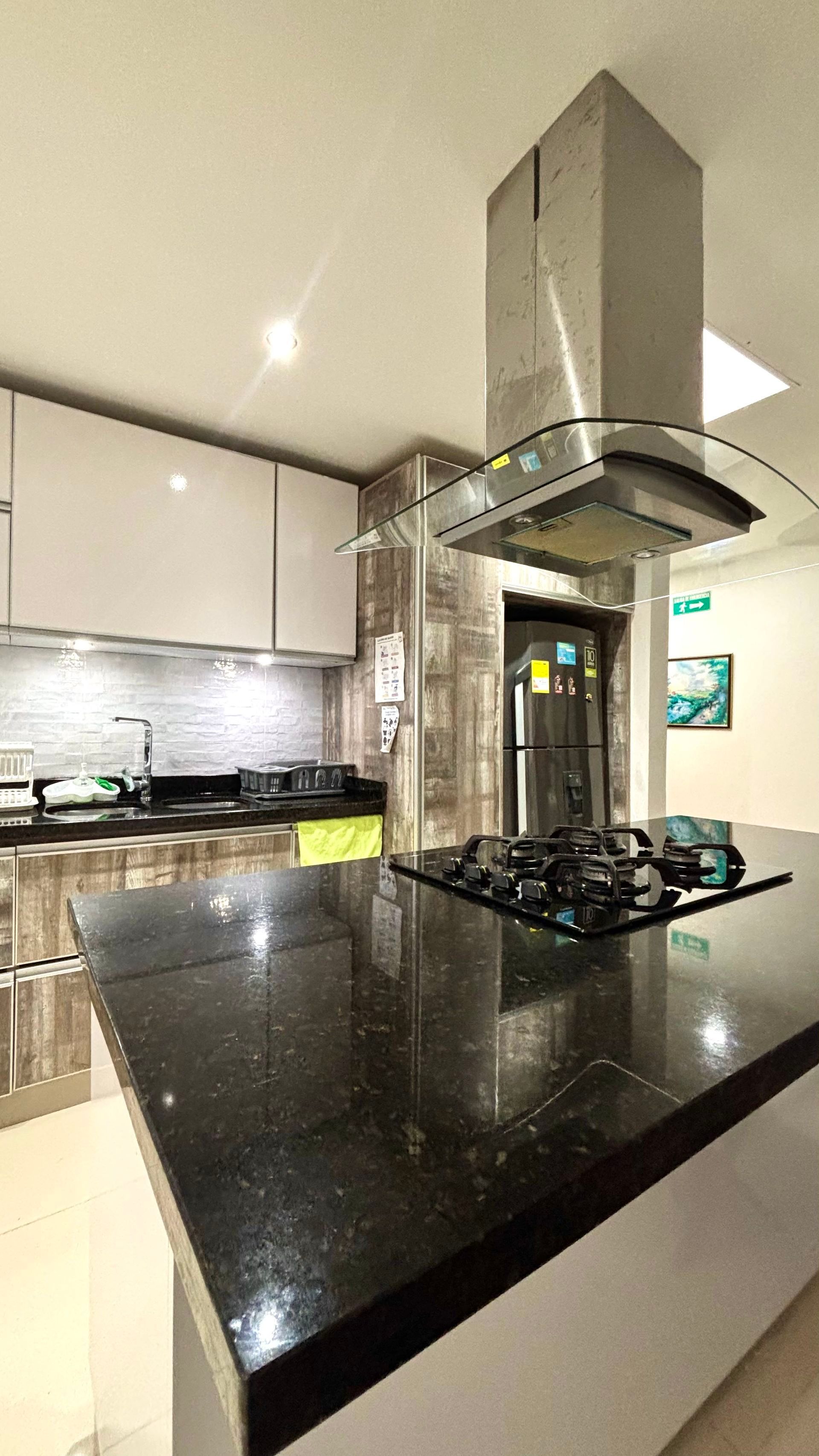 Cocina moderna con isla de granito negro, placa de gas, campana extractora de acero inoxidable y armarios blancos.